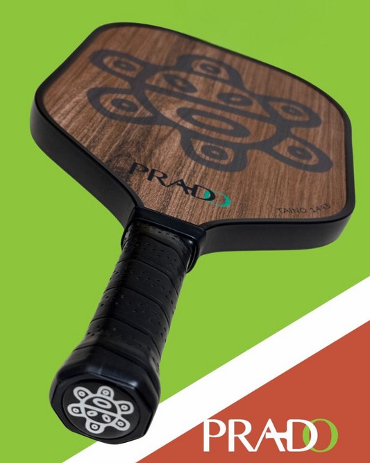 Taino Sun Paddle premium pickleball paddle with T700 carbon fiber, textured surface, and Puerto Rican cultural Taino Sun design on wooden face against green background