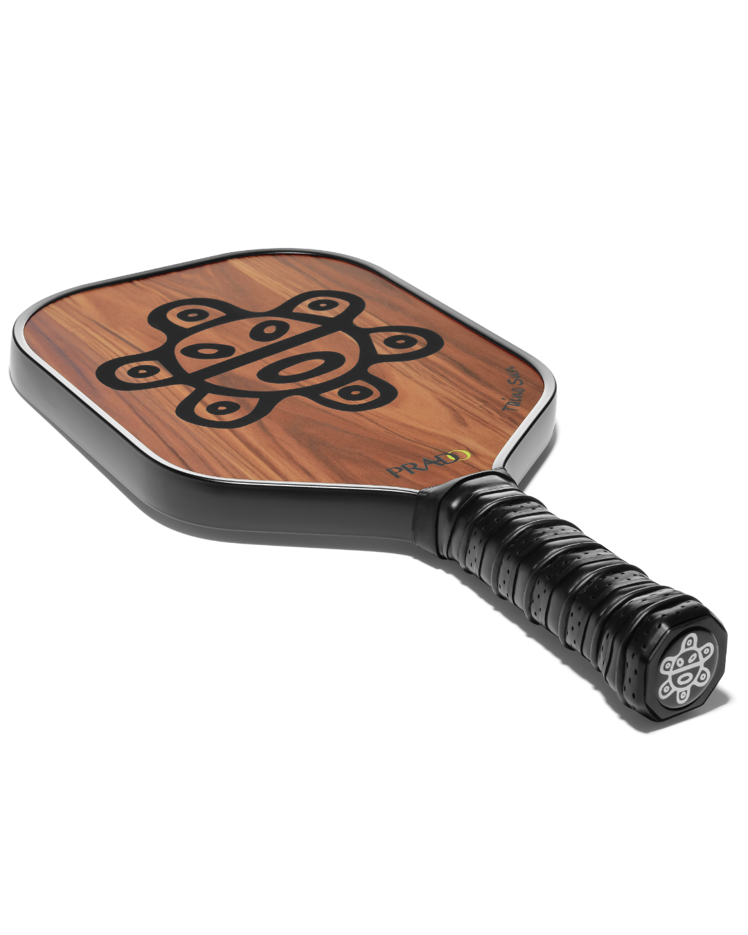 A close-up studio shot of a Taino Sun pickleball paddle on a white background, showing a warm brown wood grain face with a black geometric logo, the PRADO brand name, and a black textured grip.